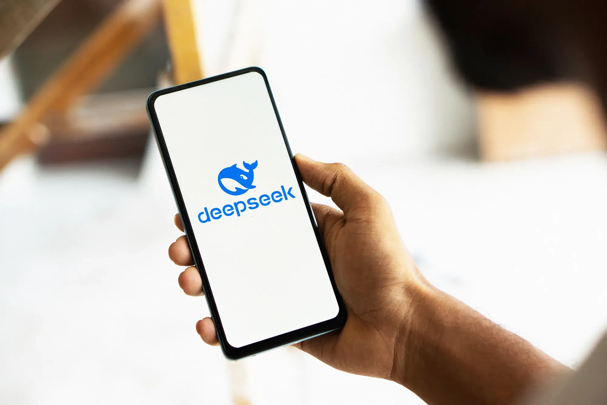 Person holding phone displaying blue DeepSeek logo with whale icon on white screen.