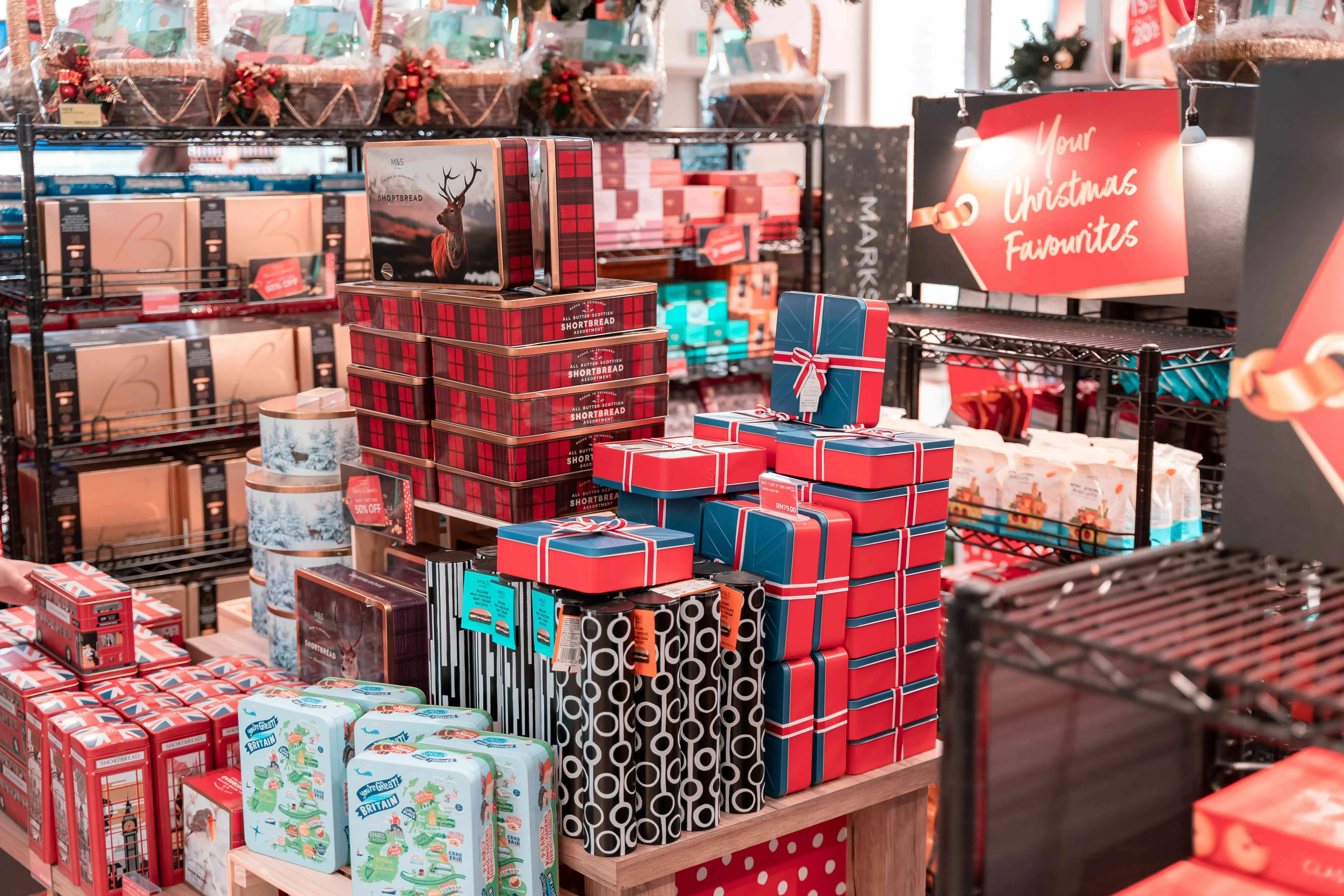 Display of stacked holiday gift boxes and shortbread tins in a Christmas-themed retail store.