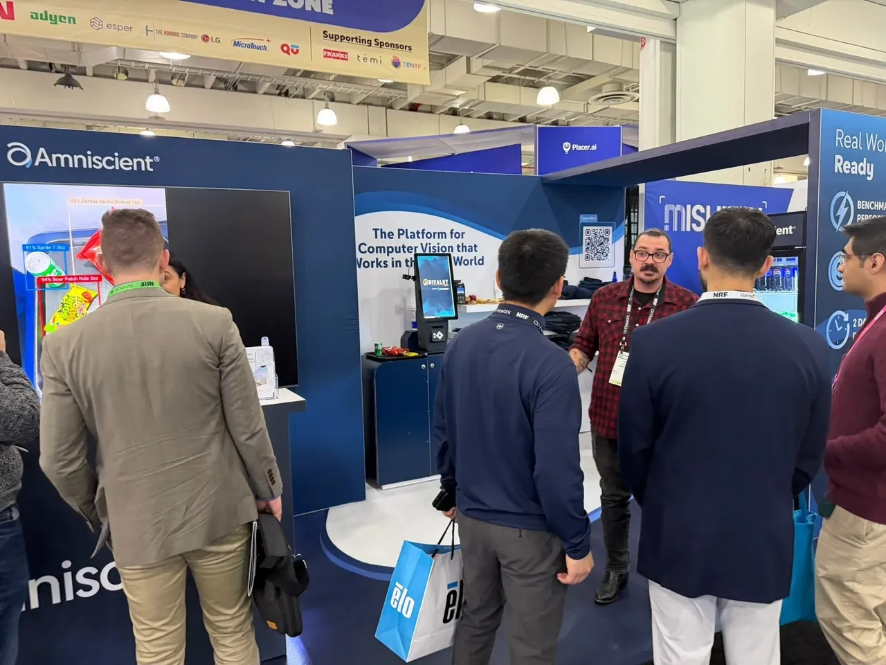 People at Amniscient booth discussing technology at a trade show or conference.